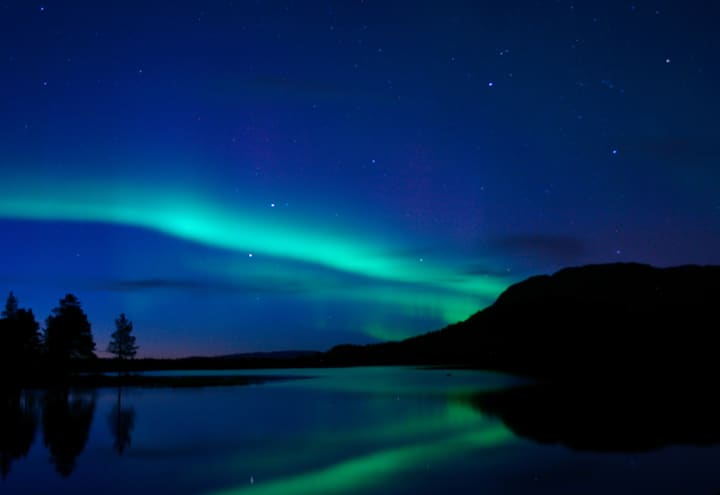 Green northern lights arc reflected in a still northern lake on a clear night