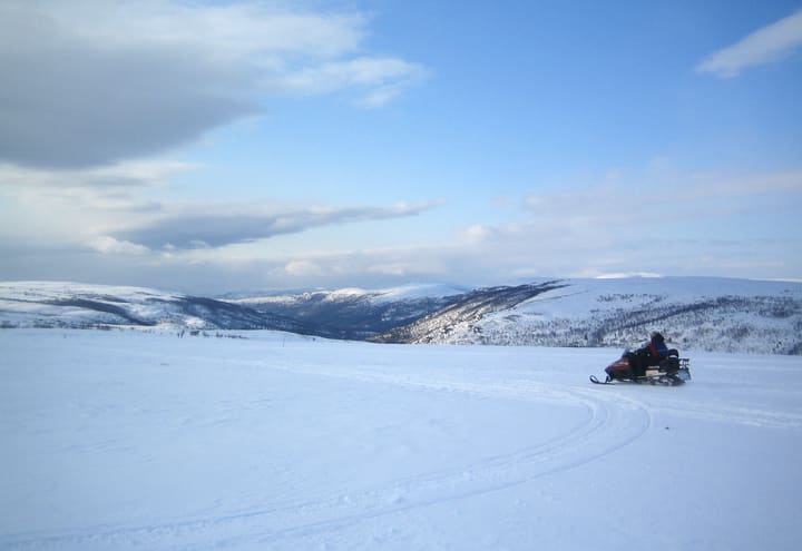Snowmobile crossing the open snow of the Finnmark plateau above Alta under a blue sky