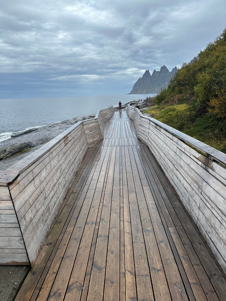 Wooden boardwalk along a Norwegian coast below steep mountains